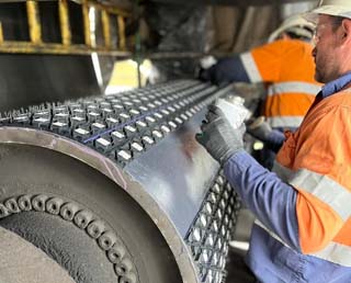 Technician installing cold-bonded pulley lagging on conveyor pulley onsite
